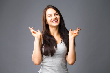 Beden dili ve duygular kavramı. Memnun koyu saçlı güzel memnun kız beggs Tanrı ona yardım için parmak çarpı işareti tutar, iyi şanslar diliyor, gri studio arka plan üzerinde kapalı izole dua ediyor.