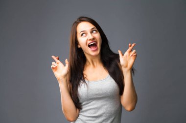 Beden dili ve duygular kavramı. Memnun koyu saçlı güzel memnun kız beggs Tanrı ona yardım için parmak çarpı işareti tutar, iyi şanslar diliyor, gri studio arka plan üzerinde kapalı izole dua ediyor.