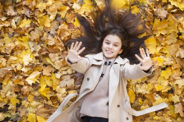Güzel küçük bir kız parkta yapraklarda güzel sonbahar gününde yatıyor