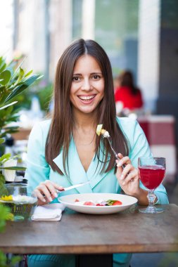 Genç güzel esmer kadın bir kafede yaz sokak açık havada kahvaltı yapıyor