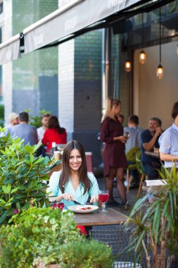 Genç güzel esmer kadın bir kafede yaz sokak açık havada kahvaltı yapıyor