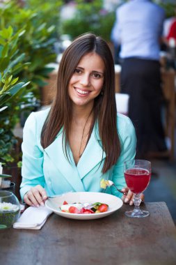 Genç güzel esmer kadın bir kafede yaz sokak açık havada kahvaltı yapıyor