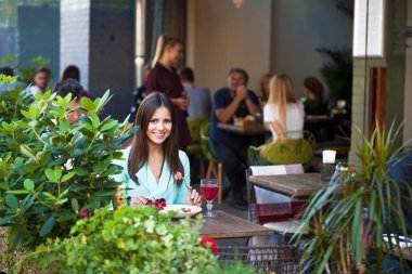 Genç güzel esmer kadın bir kafede yaz sokak açık havada kahvaltı yapıyor