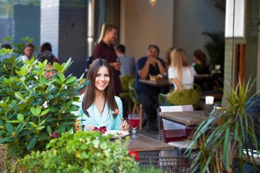 Genç güzel esmer kadın bir kafede yaz sokak açık havada kahvaltı yapıyor