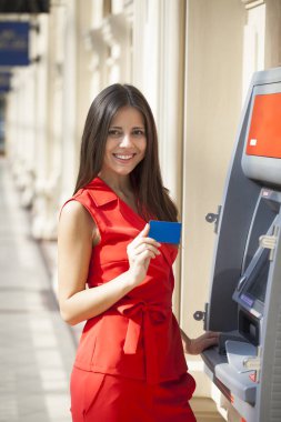 Atm de kredi kartından para çekme Kırmızı elbiseli genç mutlu esmer kadın 