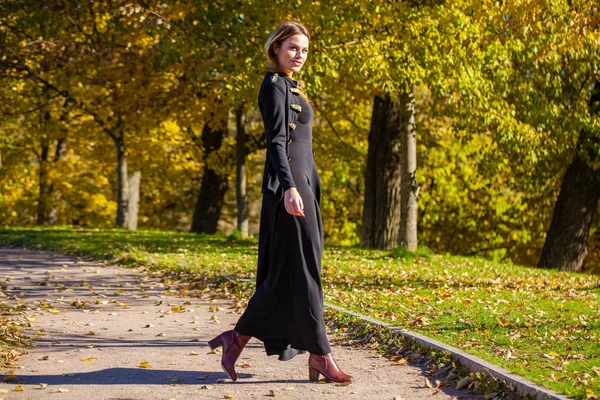 美丽的年轻金发碧眼的女人在黑色礼服走在秋天公园 — 图库照片