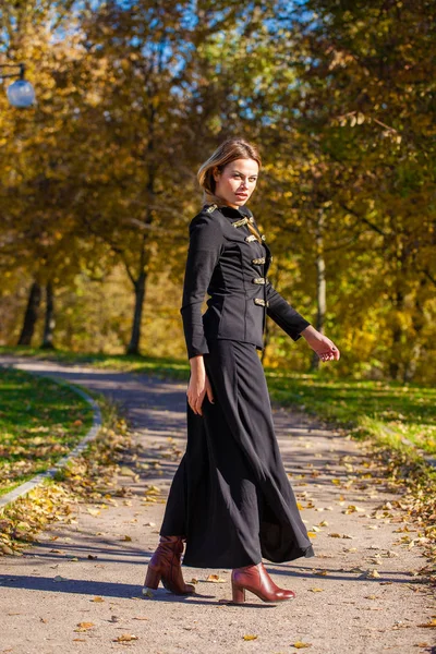 秋の公園を歩く黒のドレスで美しい若いブロンドの女性 — ストック写真