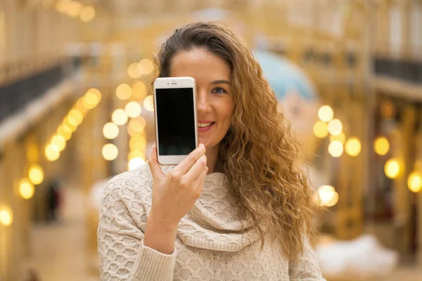 ゴールデン屋内 スマート フォン画面を示す若い美しいカーリー ブロンドの女性 — ストック写真