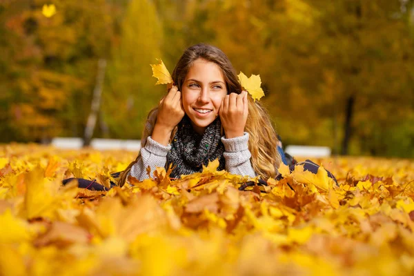 美しい小さな女の子が美しい秋の日に公園で葉に横たわり — ストック写真