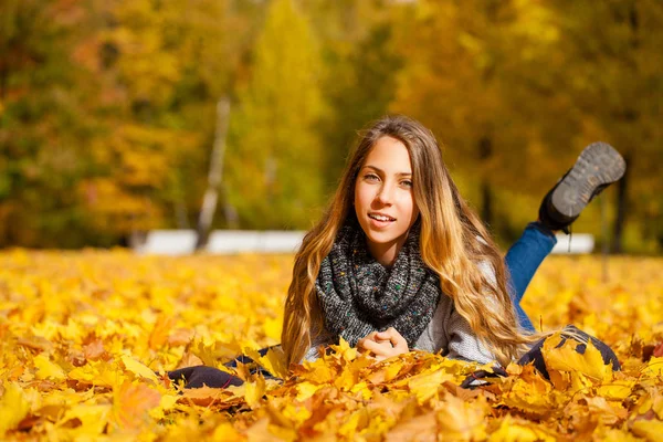 美しい小さな女の子が美しい秋の日に公園で葉に横たわり — ストック写真