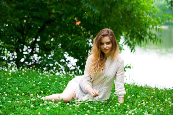 性感年轻的金发女子 穿白色连衣裙坐在绿草中夏公园 — 图库照片