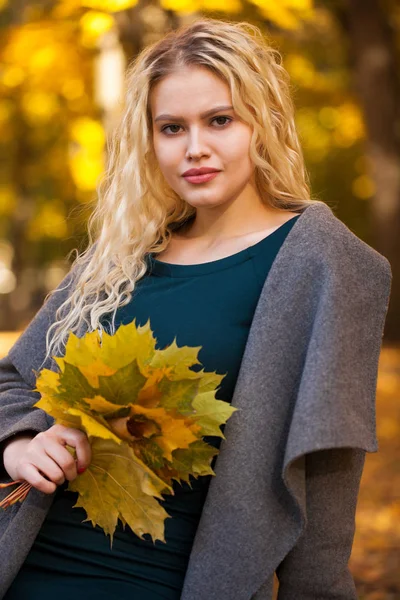 在秋天街头的背景上的灰色外套年轻金发美女的画像 — 图库照片