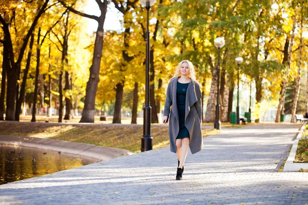 秋の公園を歩いてグレーのコートを着た若い美しい金髪のセクシーな女性 — ストック写真