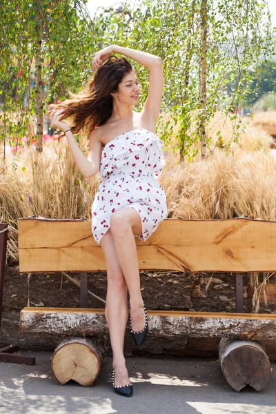 完全な成長の通り夏の屋外木製のベンチに座って白いドレスの若い美しいブルネットの女性の肖像画 — ストック写真