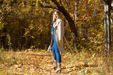 Güzel sarışın kız bir sonbahar park, sarı ve turuncu bir tam uzunlukta ile bej bir palto bırakır 