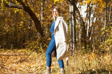 Güzel sarışın kız bir sonbahar park, sarı ve turuncu bir tam uzunlukta ile bej bir palto bırakır 