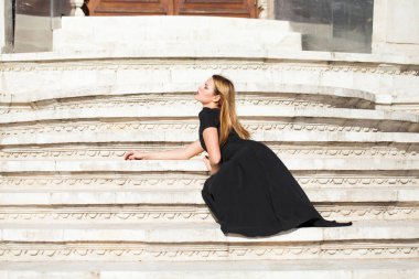 Tam uzunlukta taş merdiven üstünde oturan uzun siyah elbise genç güzel sarışın kadın portresi