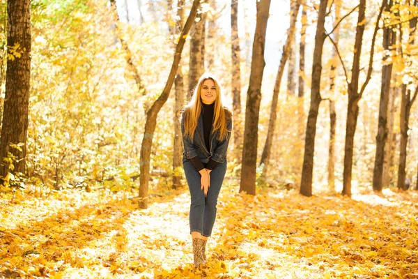 Full portrait of Stylish young blonde woman in blue denim overalls in autumn park