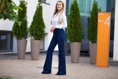 Kot pantolon ve beyaz gömlekli, uzun boylu, güzel bir iş kadınının portresi.