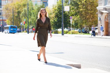 Tam büyüme portre, genç güzel sarışın kadın koyu yeşil elbise sokakta yaz açık havada yürüyüş