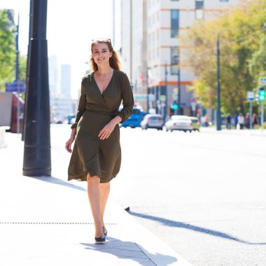 Tam büyüme portre, genç güzel sarışın kadın koyu yeşil elbise sokakta yaz açık havada yürüyüş