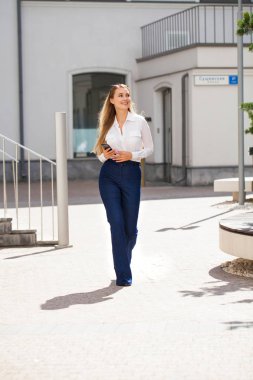 Kot pantolon ve beyaz gömlekli, uzun boylu, güzel bir iş kadınının portresi.