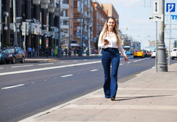 Kot pantolon ve beyaz gömlekli, uzun boylu, güzel bir iş kadınının portresi.