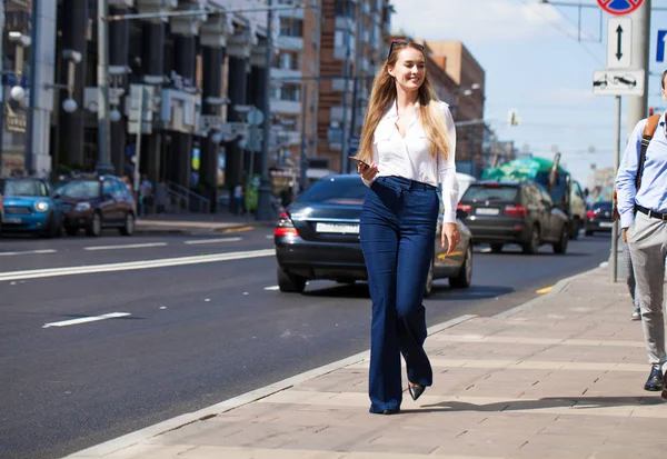 Kot pantolon ve beyaz gömlekli, uzun boylu, güzel bir iş kadınının portresi.