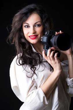 Koyu arka plan üzerinde kamera tutan mutlu esmer fotoğrafçı kadın