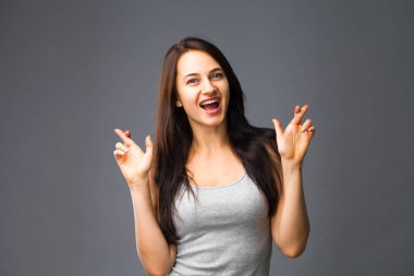 Beden dili ve duygular kavramı. Memnun koyu saçlı güzel memnun kız beggs Tanrı ona yardım için parmak çarpı işareti tutar, iyi şanslar diliyor, gri studio arka plan üzerinde kapalı izole dua ediyor.