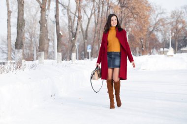 Tam vücut. Genç güzel esmer kadın kırmızı paltolu kış park üzerinde poz. Şık sıcak giysiler giyen modeli.