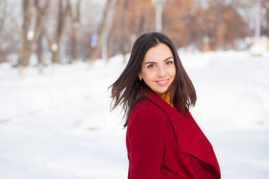 Genç güzel esmer kadın kırmızı paltolu kış park üzerinde poz. Şık sıcak giysiler giyen modeli.