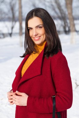 Genç güzel esmer kadın kırmızı paltolu kış park üzerinde poz. Şık sıcak giysiler giyen modeli.