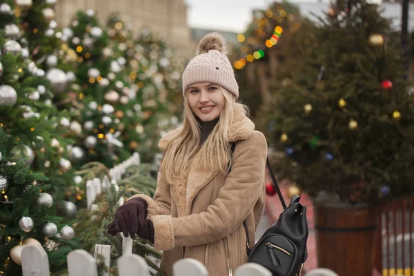 快乐美丽的金发碧眼的女人在羊皮外套和针织帽子在圣诞庭院的中心 — 图库照片
