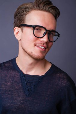 Karanlık bir arka plan üzerinde büyük gözlüklü genç bir adam portresi stüdyo