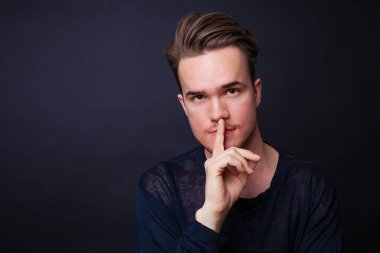 Genç adam sessizlik jest koyu arka plan üzerinde gösterilen. 