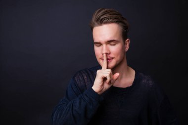 Genç adam sessizlik jest koyu arka plan üzerinde gösterilen. 