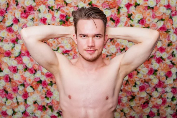 Portrait of a young sexy guy on the background of floral studio wall