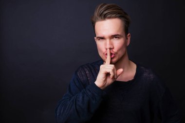Genç adam sessizlik jest koyu arka plan üzerinde gösterilen. 