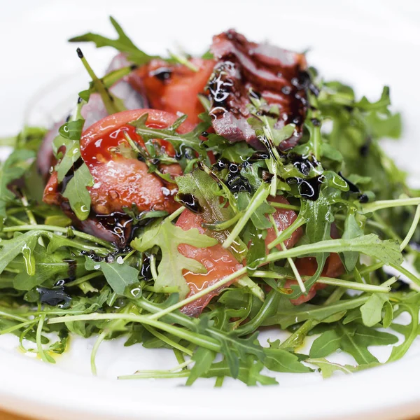 Sallad med bitar av marmorerat nötkött och ruccola på en vit platta — Stockfoto