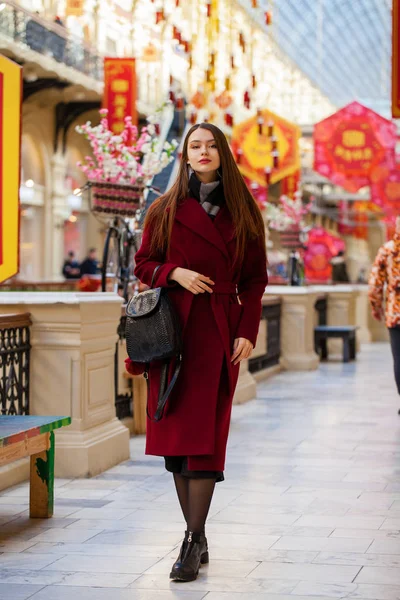 Όμορφο κορίτσι στο κομψό σε ένα μακρύ Μπορντό παλτό, εσωτερική κατάστημα — Φωτογραφία Αρχείου