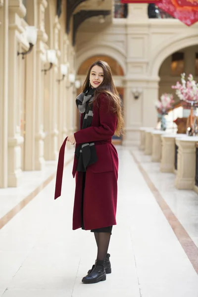 Menina bonita em elegante em um casaco longo Borgonha, loja de interior — Fotografia de Stock