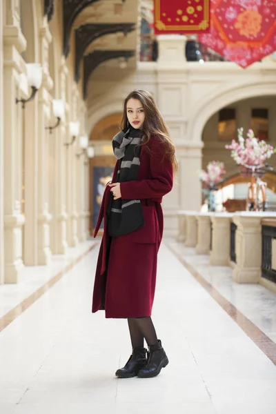 Bella ragazza in elegante in un lungo cappotto bordeaux, negozio al coperto — Foto Stock