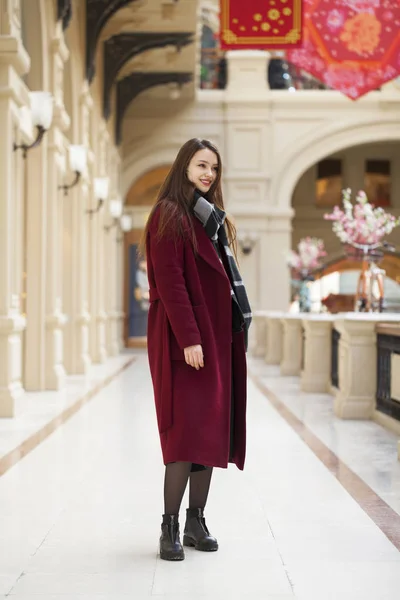 A szép lány a stílusos egy hosszú bordó kabátot, fedett shop — Stock Fotó