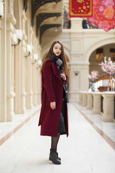 Hermosa chica con estilo en un abrigo largo de color burdeos, tienda interior —  Fotos de Stock