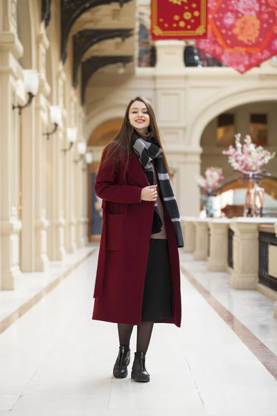 Bella ragazza in elegante in un lungo cappotto bordeaux, negozio al coperto — Foto Stock