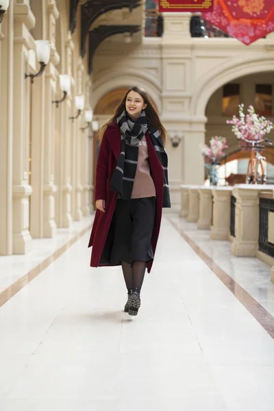 Krásná dívka ve stylové v dlouhé vínové kabátě, vnitřní obchod — Stock fotografie