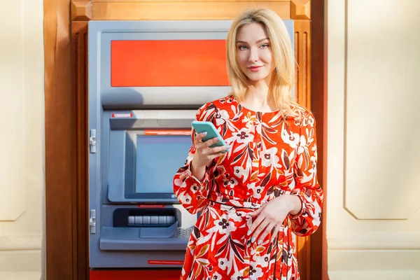 Happy blonde woman withdrawing money from credit card at ATM