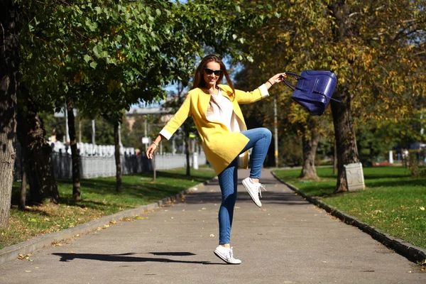 Glückliche Frau in gelbem Mantel spaziert durch die Herbststraße — Stockfoto