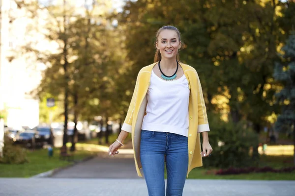 Happy young woman in yellow coat in autumn street — Stock Photo, Image
